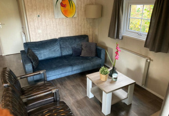 Stue i Boslodge 4 på De Utrechtse Heuvelrug, Holland, med blå sofa, lænestole og et lille sofabord.