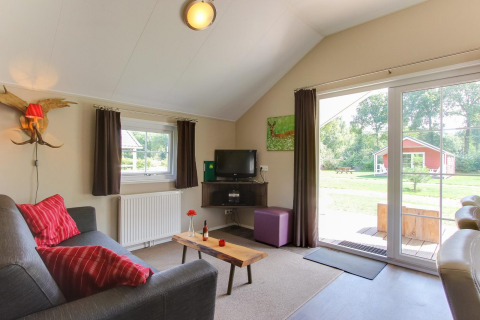 Wohnzimmer in Boslodge 4 in De Utrechtse Heuvelrug, Niederlande, mit Sofa, Fernseher und Blick nach draußen.
