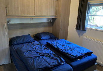 Schlafzimmer in Boslodge 4 im De Utrechtse Heuvelrug, Niederlande, mit zwei Einzelbetten und blauer Bettwäsche.