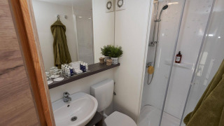 Modern bathroom in Glampingtent 6 featuring a shower, sink, toilet, mirror, green towels and toiletries.