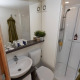 Moderne badeværelse i Glampingtent 6 med brusekabine, håndvask, toilet, spejl og grønne håndklæder.