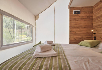 Interior view of Glampingtent 6 at De Utrechtse Heuvelrug, Netherlands, showing cozy bed and large window.