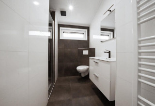 Modernes Badezimmer in einer Lodge mit wandhängender Toilette, Dusche, Fenstern und weißem Waschbeckenunterschrank.