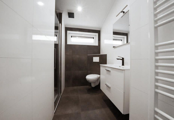 Baño moderno en un lodge con inodoro suspendido, ducha, ventanas y armario blanco debajo del lavabo.