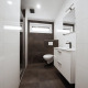Moderne badeværelse på en lodge med væghængt toilet, bruser, vinduer og hvide skabe under vasken.