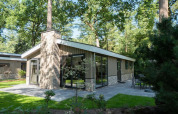 Modern lodge with large windows and patio, surrounded by trees and greenery in a peaceful forest setting.