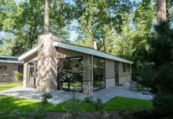Moderne lodge met grote ramen en terras, midden in het groen en omgeven door bomen in een bosrijke omgeving.