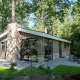 Moderne Lodge mit großen Fenstern und Terrasse, umgeben von Bäumen und Natur in einem Waldgebiet.