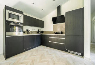 Moderne Lodge-Küche mit schwarzen Holzfronten, integrierten Geräten und hellem Fischgrätparkettboden.