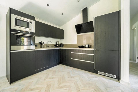 Cocina moderna en una cabaña, con muebles negros, electrodomésticos integrados y suelo de espiga claro.