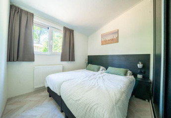 Chambre lumineuse dans un lodge avec deux lits simples, coussins verts et grande fenêtre à rideaux gris.