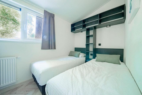Dormitorio luminoso de lodge con dos camas individuales, grandes ventanas y estanterías sobre las camas.