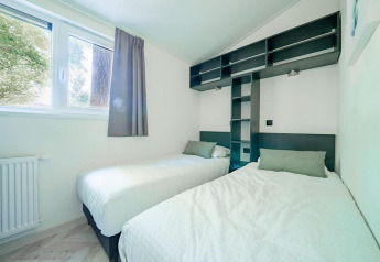 Helles, modernes Schlafzimmer in einer Lodge mit zwei Einzelbetten, großen Fenstern und Regalwand.