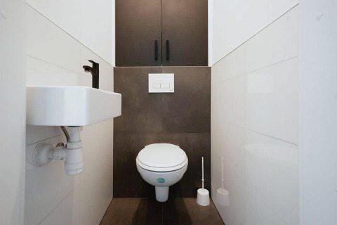 Aseo moderno de lodge con inodoro mural, lavabo compacto y armario oscuro en un espacio estrecho.