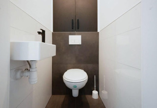 Moderne lodge-toilet met zwevend toilet, compacte lavabo en donkere kast in een smalle ruimte.