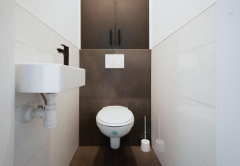 Modernes Lodge-Bad mit Wandtoilette, kleinem Waschbecken und dunklen Schränken in engem Raum.