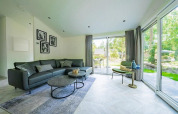 Modern lodge living room with large windows, gray sofa, coffee tables, armchair, and garden view outside.