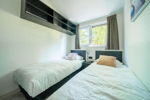 Heldere lodge slaapkamer met twee aparte bedden, een groot raam en moderne inrichting en kussens.