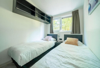 Heldere lodge slaapkamer met twee aparte bedden, een groot raam en moderne inrichting en kussens.