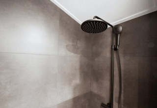 Ducha negra moderna en el baño de una cabaña con grandes azulejos grises en paredes y techo.