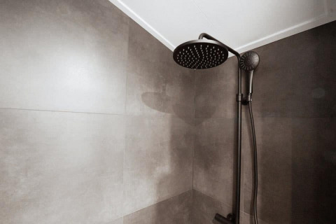 Ducha negra moderna en el baño de una cabaña con grandes azulejos grises en paredes y techo.