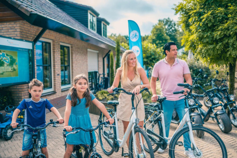Gezin aan een glamping accommodatie, klaar voor een fietstocht op een zonnige dag, omringd door natuur.