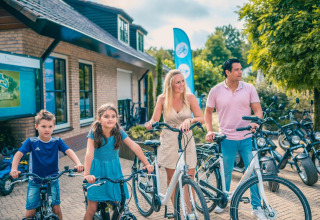 Gezin aan een glamping accommodatie, klaar voor een fietstocht op een zonnige dag, omringd door natuur.