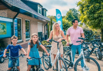 Familie ved glamping indkvartering, klar til at tage på cykeltur på en solrig dag, omgivet af natur.