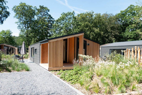 Panorama Cottage 4-lodge med moderne træfacade og grøn have, omgivet af natur og andre hytter.