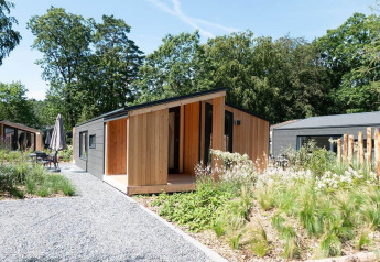 Panorama Cottage 4-lodge med moderne træfacade og grøn have, omgivet af natur og andre hytter.