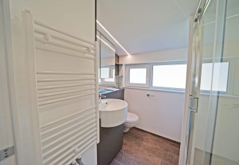 Moderne badkamer met houtlook vloer, wastafel, grote spiegel, douche en ramen in Panorama Cottage 4, Nederland.