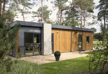 Lodge moderno in legno e cemento immerso nella foresta, con ampie finestre e prato ben curato.