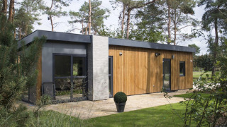 Lodge moderne en bois et béton niché dans une forêt, avec de grandes fenêtres et une pelouse bien entretenue.