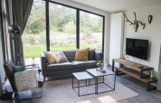 Sala de glamping moderna con grandes ventanales, sofá negro, vista natural y astas decorativas en la pared.