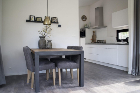 Modern glamping accommodation featuring a cozy dining table, comfy chairs, and a sleek, bright kitchen.