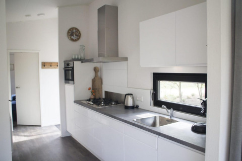 Moderne lodgekeuken met witte kasten, ingebouwde oven, gaskookplaat en een raam met uitzicht buiten.