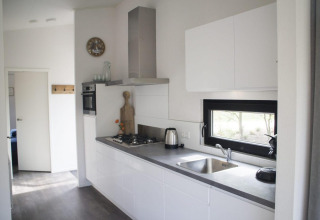 Moderne lodgekeuken met witte kasten, ingebouwde oven, gaskookplaat en een raam met uitzicht buiten.