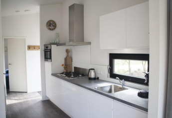 Cuisine moderne d’un lodge avec armoires blanches, électroménagers intégrés et fenêtre sur la nature.