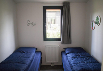 Camera da glamping con due letti singoli, biancheria blu e una finestra centrale con tenda grigia.