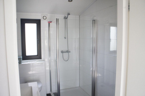 Baño moderno en alojamiento glamping con ducha de cristal, azulejos blancos y ventana luminosa.
