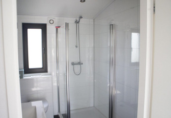 Bagno moderno in una sistemazione glamping con doccia in vetro, piastrelle bianche e finestra luminosa.