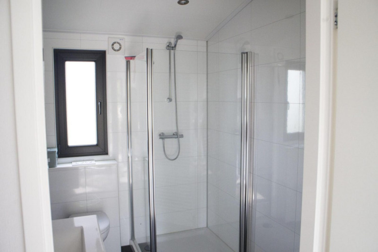 Modern bathroom at a glamping accommodation featuring a glass shower, white tiles, and a window.