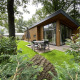 Moderne Pavilion 6 lodge med træfacade, store vinduer, havebord og parasol i omgivet grøn natur.