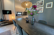 Dining room with dark table, flower vase, stylish lighting, and kitchen in Pavilion 6, De Utrechtse Heuvelrug.