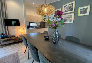 Eetkamer met donkere tafel, vaas bloemen en keuken in Pavilion 6, De Utrechtse Heuvelrug in Nederland.