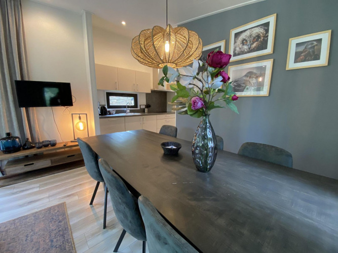 Dining room with dark table, flower vase, stylish lighting, and kitchen in Pavilion 6, De Utrechtse Heuvelrug.