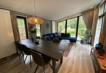Moderne woonkamer in Pavilion 6 bij De Utrechtse Heuvelrug, Nederland, met grote ramen en blauwe zetel.
