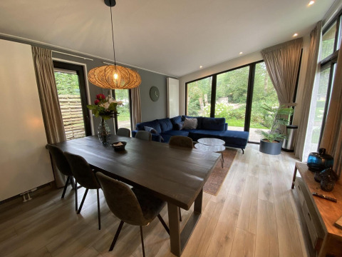 Modern living room in Pavilion 6 at De Utrechtse Heuvelrug, Netherlands, with large windows and blue sofa.