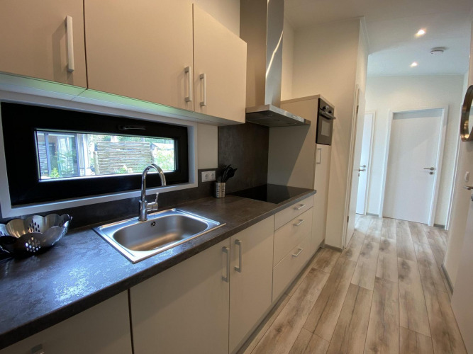 Modern kitchen setup in Pavilion 6 at De Utrechtse Heuvelrug, Netherlands, featuring wood flooring and window.