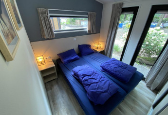 Moderne slaapkamer met tweepersoonsbed, blauwe lakens en grote ramen in Pavilion 6, De Utrechtse Heuvelrug.